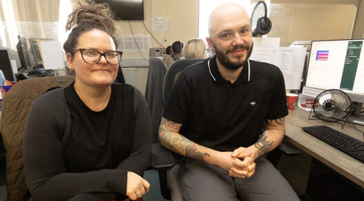 a woman and a man sitting in an office with computer screens behind them