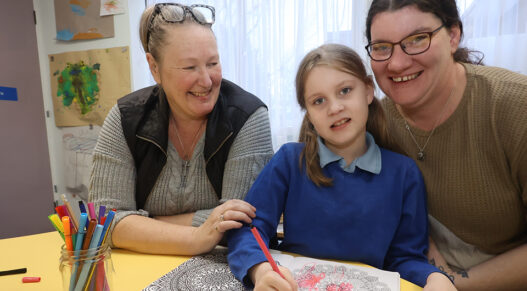 A girls plays with drawing pens, with her mother right and another woman left